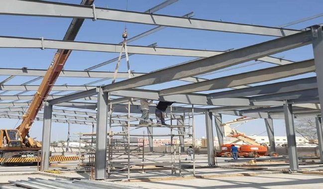 Warehouse steel frame being erected with a crane and lift
