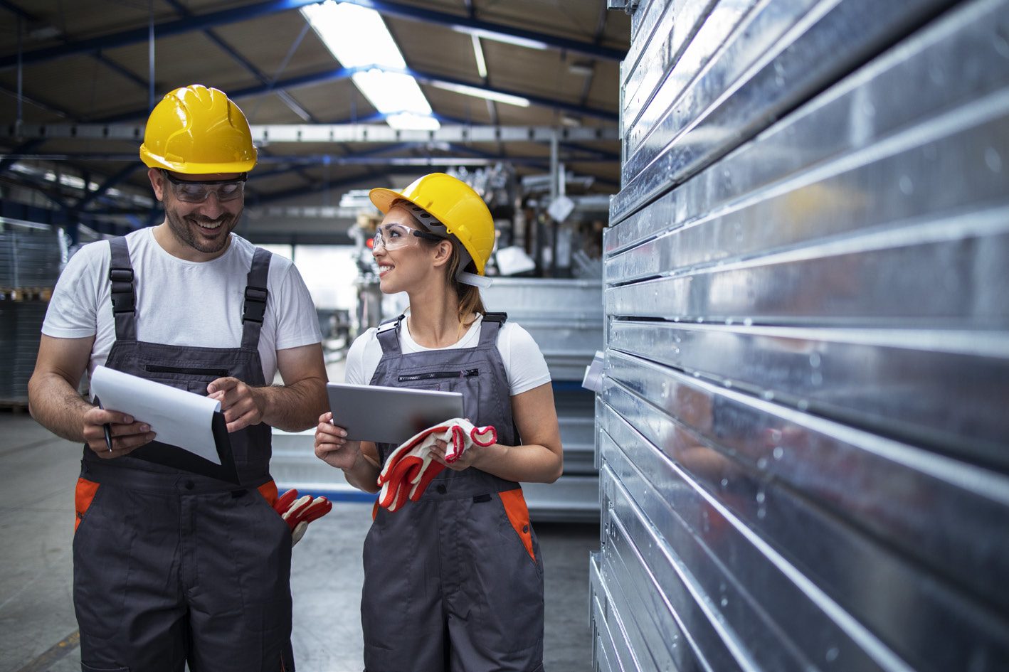 Two engineers in hard hats reviewing drawings in a steel workshop