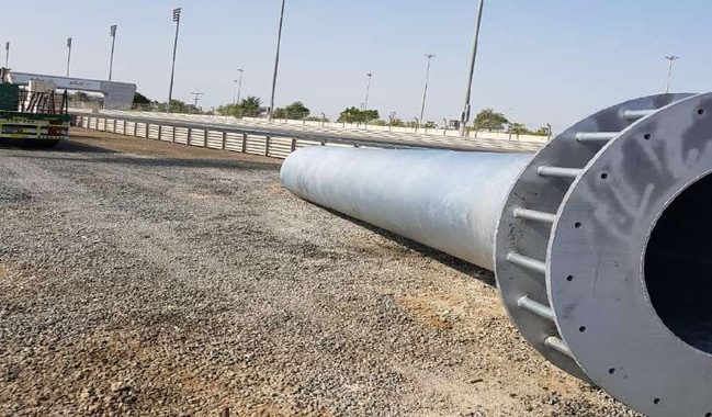 Large fabricated steel pole with base plate lying on gravel